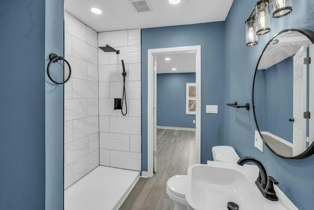 full bath with wood finished floors, visible vents, tiled shower, and a sink