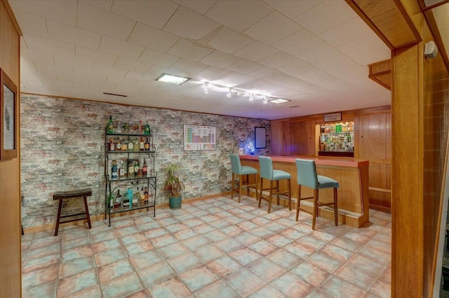 bar with a bar, wood walls, light floors, and rail lighting