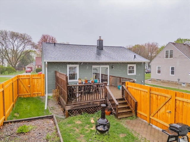rear view of property with a chimney, a lawn, a wooden deck, a fenced backyard, and a shingled roof