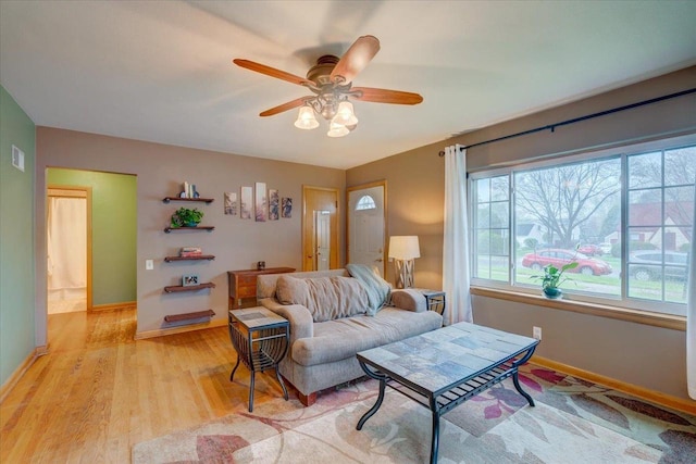 living area with a ceiling fan, baseboards, and light wood-type flooring
