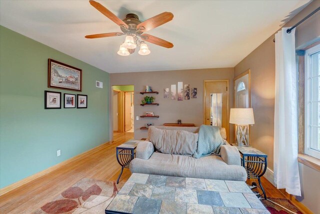 living area with baseboards, a ceiling fan, wood finished floors, and visible vents