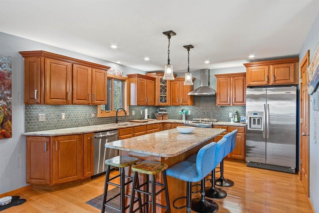 W4895 Big Bay Rd, Necedah, WI 54646 - kitchen featuring stainless steel appliances, wall chimney exhaust hood, a sink, brown cabinetry, and a kitchen breakfast bar