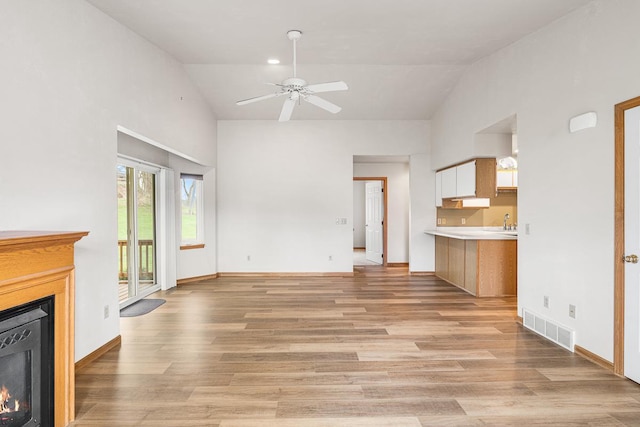 unfurnished living room with a warm lit fireplace, ceiling fan, high vaulted ceiling, visible vents, and light wood-style flooring