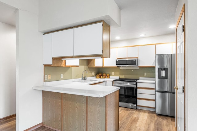 kitchen featuring a sink, stainless steel appliances, light wood-style flooring, a peninsula, and light countertops