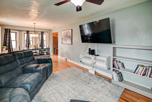 living room featuring baseboards, wood finished floors, and ceiling fan with notable chandelier
