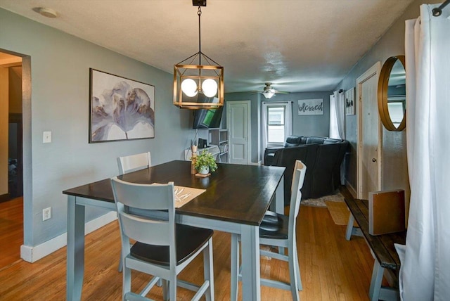 dining space featuring light wood-style floors, baseboards, and ceiling fan with notable chandelier