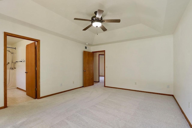 empty room featuring a raised ceiling, a ceiling fan, baseboards, and light carpet