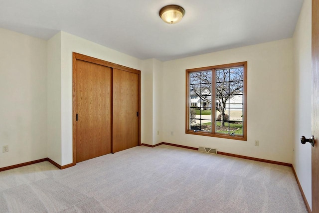 unfurnished bedroom with light colored carpet, visible vents, baseboards, and a closet