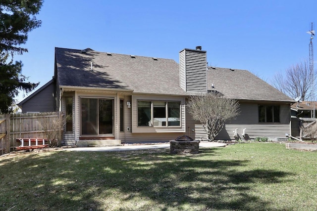 back of house featuring a shingled roof, an outdoor fire pit, a lawn, a chimney, and fence