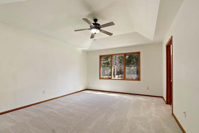 carpeted empty room featuring a raised ceiling, ceiling fan, and baseboards