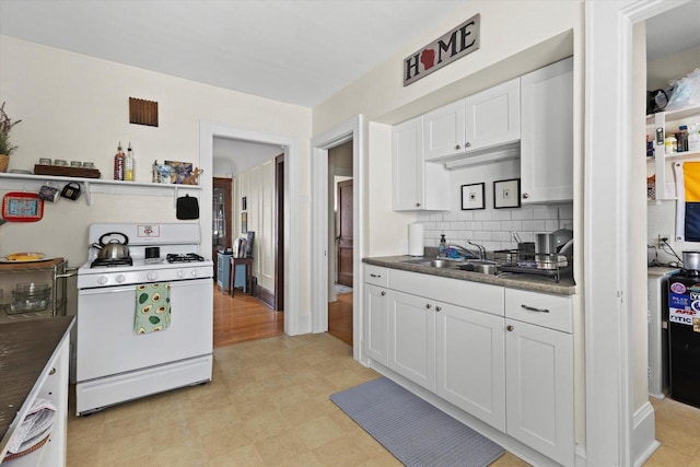 kitchen featuring a sink, white gas range oven, tasteful backsplash, white cabinetry, and light floors