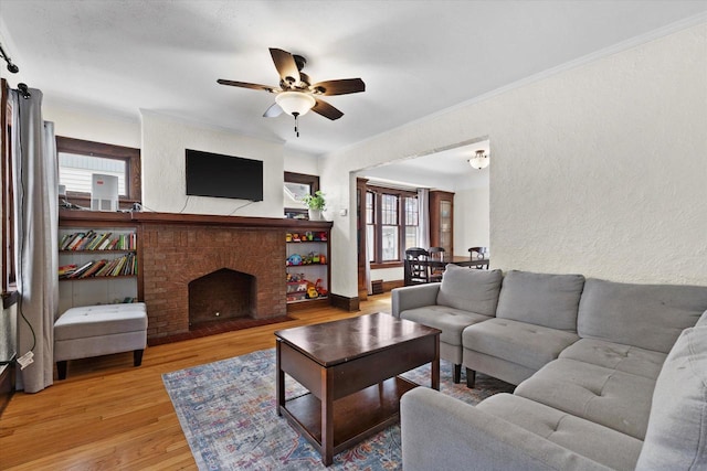 living area featuring a textured wall, ceiling fan, ornamental molding, a brick fireplace, and wood finished floors