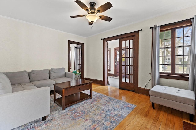 living area with ornamental molding, ceiling fan, light wood finished floors, baseboards, and french doors