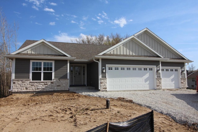 view of front facade featuring a garage, board and batten siding, gravel driveway, and stone siding