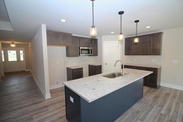 kitchen with backsplash, stainless steel microwave, dark brown cabinets, and a sink
