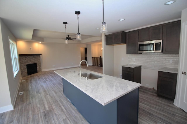 kitchen with stainless steel microwave, a sink, a fireplace, tasteful backsplash, and dark brown cabinets