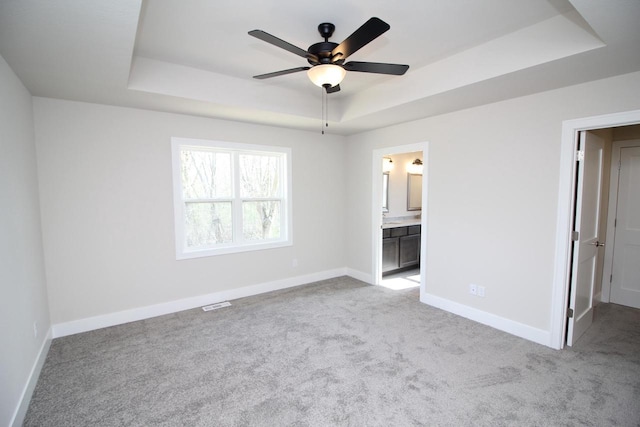 unfurnished bedroom with carpet floors, ensuite bathroom, baseboards, visible vents, and a tray ceiling