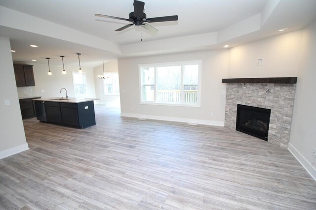 unfurnished living room featuring light wood-style flooring, ceiling fan, a fireplace, a sink, and baseboards