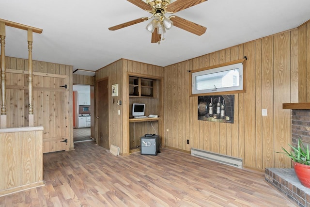 unfurnished room with wooden walls, a ceiling fan, baseboard heating, and wood finished floors