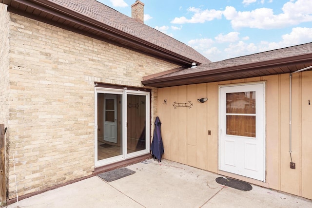 entrance to property featuring roof with shingles, a chimney, a patio area, and board and batten siding