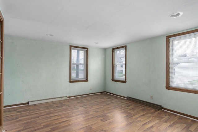empty room with recessed lighting, wood finished floors, a baseboard radiator, baseboards, and visible vents