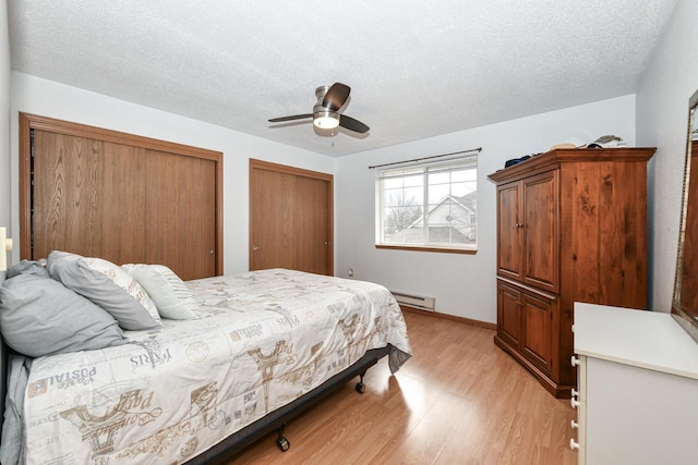 bedroom with a baseboard heating unit, two closets, light wood-type flooring, a ceiling fan, and a textured ceiling
