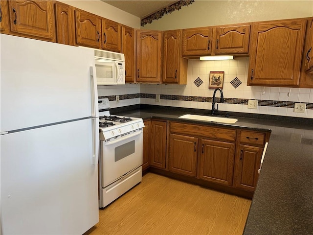 kitchen featuring decorative backsplash, dark countertops, white appliances, light wood-type flooring, and a sink