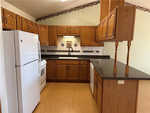 kitchen featuring a sink, dark countertops, light wood-type flooring, and white appliances