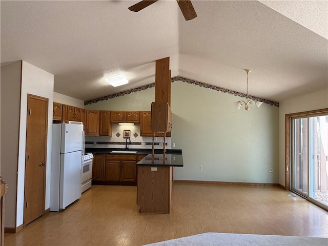 kitchen featuring dark countertops, a sink, white appliances, a peninsula, and lofted ceiling
