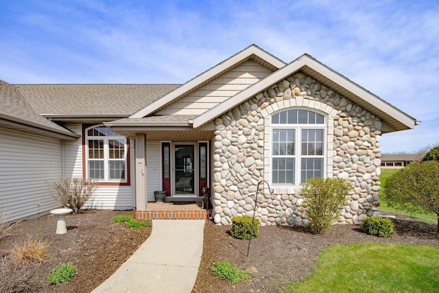 view of exterior entry featuring stone siding, covered porch, and roof with shingles