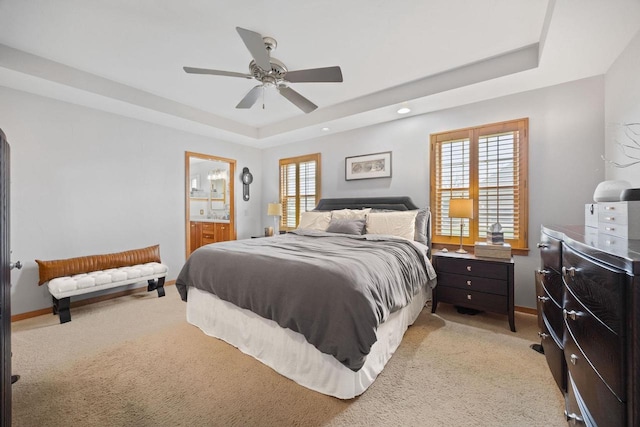 bedroom featuring ceiling fan, a raised ceiling, ensuite bath, baseboards, and light colored carpet