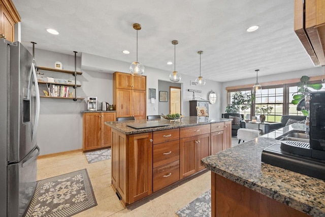 kitchen with brown cabinetry, stainless steel fridge, a kitchen island, and dark stone counters