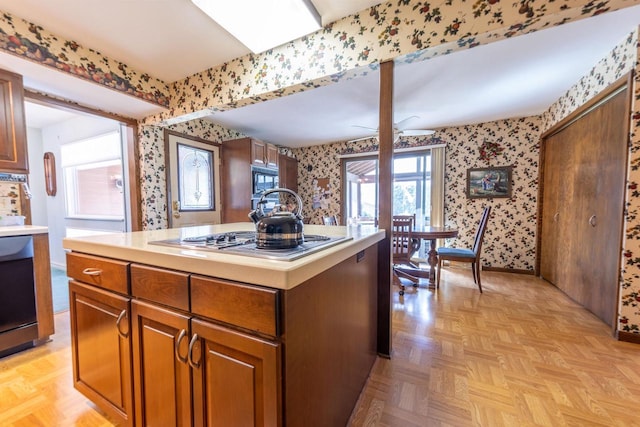 kitchen with wallpapered walls, light countertops, brown cabinets, stainless steel stovetop, and a center island