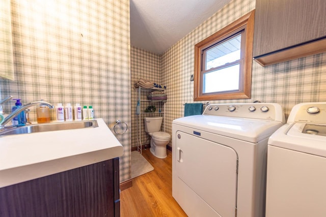 washroom with laundry area, wallpapered walls, washer and dryer, a sink, and light wood-type flooring
