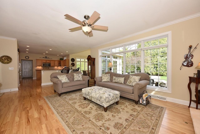 living room featuring a ceiling fan, visible vents, ornamental molding, and light wood-style floors