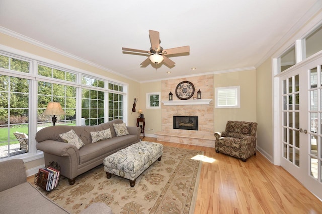 living room with crown molding, wood finished floors, baseboards, a stone fireplace, and a ceiling fan