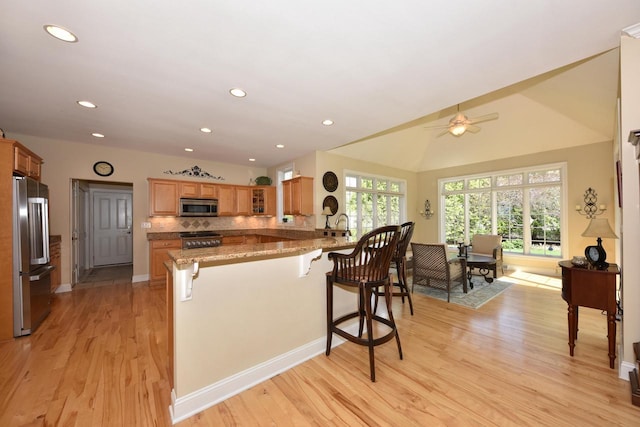 kitchen featuring light wood-type flooring, built in refrigerator, stainless steel microwave, a peninsula, and a breakfast bar