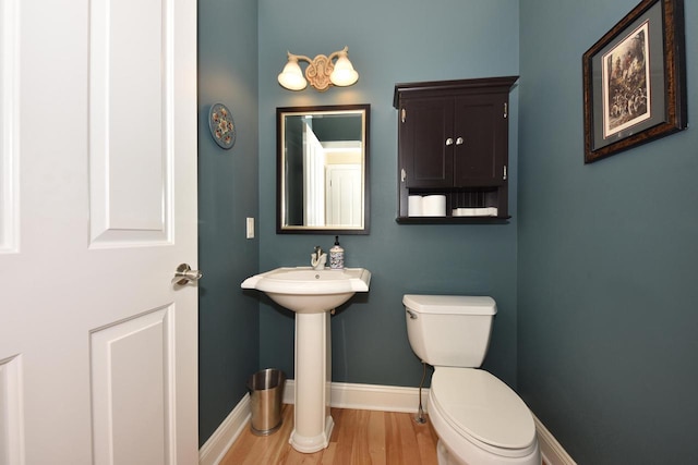 half bath with baseboards, toilet, and wood finished floors