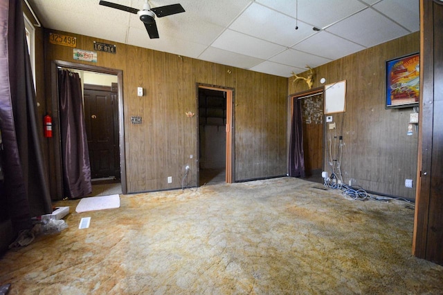 interior space with a paneled ceiling, ceiling fan, and wood walls