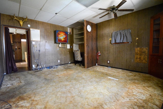 unfurnished living room featuring wood walls, a drop ceiling, and a ceiling fan