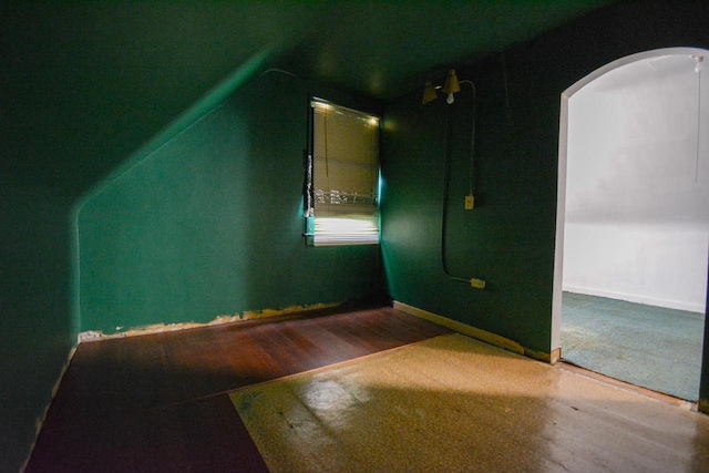 additional living space featuring wood finished floors, baseboards, vaulted ceiling, and arched walkways