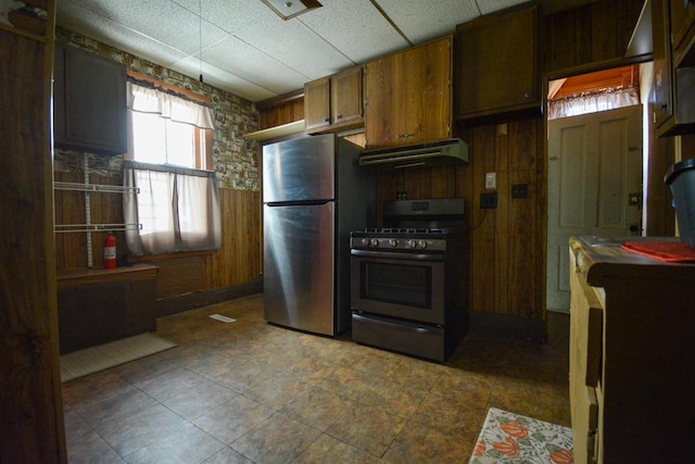 kitchen featuring wood walls, stainless steel appliances, brown cabinetry, and under cabinet range hood