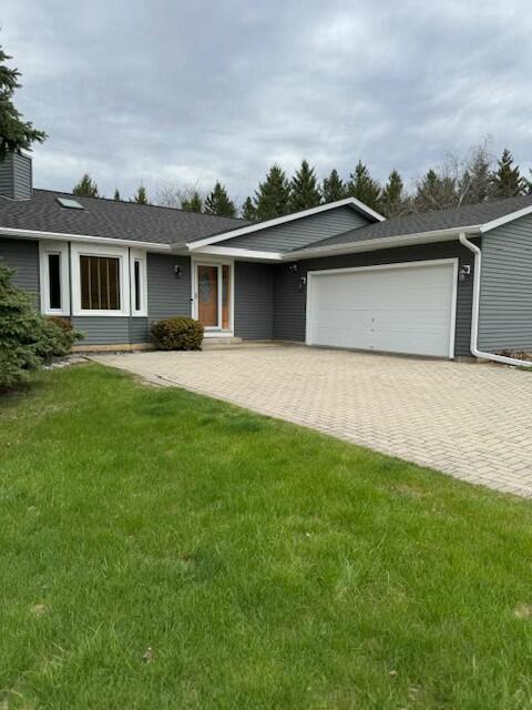 single story home with decorative driveway, a front lawn, and an attached garage
