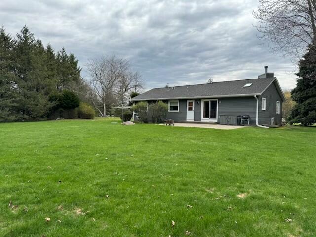 rear view of house with a chimney, a yard, and a patio