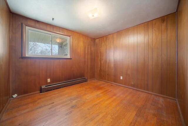 167 Gwynn St, Green Bay, WI 54301 - unfurnished room with baseboard heating, wood walls, hardwood / wood-style flooring, and baseboards