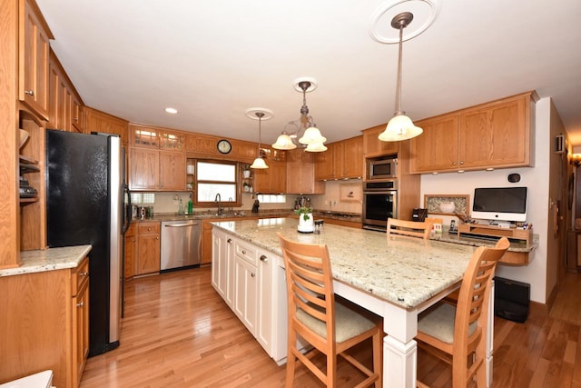 kitchen with a breakfast bar area, a sink, appliances with stainless steel finishes, light wood-style floors, and a large island
