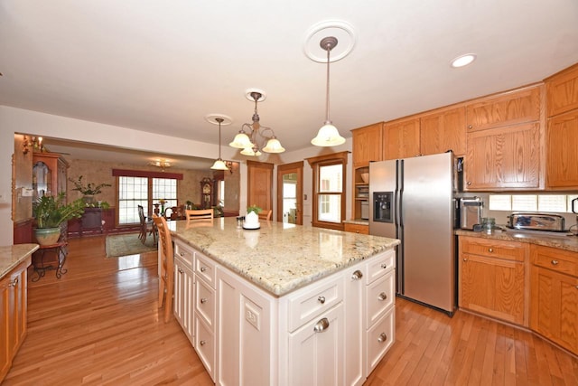 kitchen featuring a notable chandelier, a kitchen island, light wood-style flooring, pendant lighting, and stainless steel fridge with ice dispenser