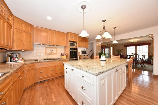 kitchen with a center island, light wood-style floors, appliances with stainless steel finishes, and decorative backsplash