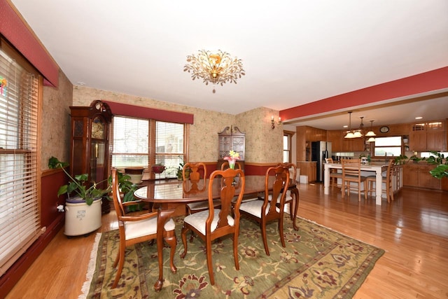 dining space with wallpapered walls, a wainscoted wall, and light wood-style floors