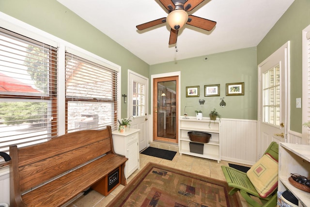 sitting room with light tile patterned floors, a wainscoted wall, and a ceiling fan